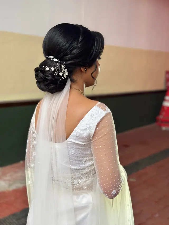 Low bridal bun with delicate white floral hair pins and a flowing veil