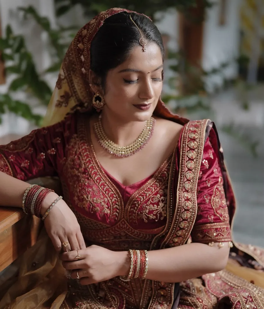 Real bride in a maroon and gold lehenga with HD bridal makeup, hair and draping by Ammu Bridal Studio