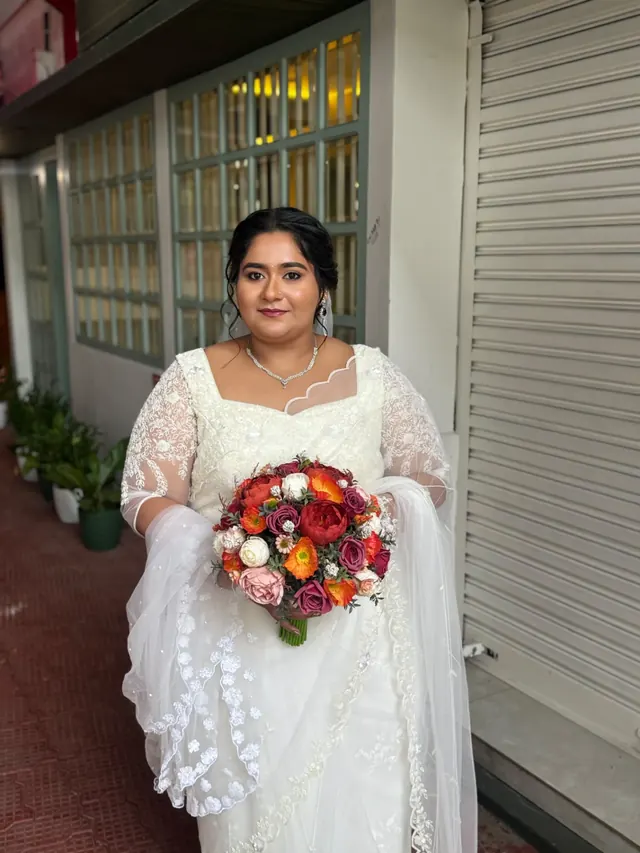 Christian bride in a white lace gown holding a red and orange floral bouquet