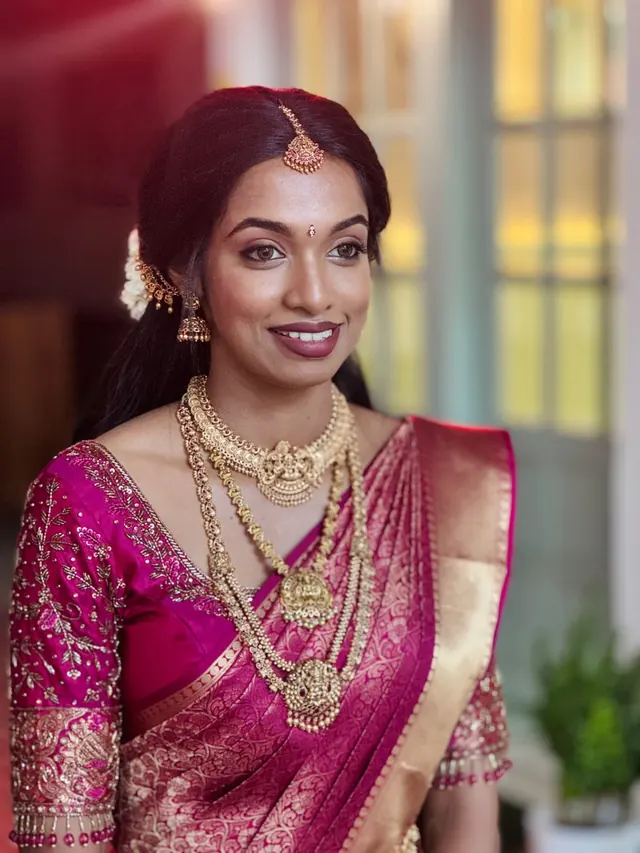 Kerala bride in a magenta silk saree with traditional gold jewellery and bridal makeup