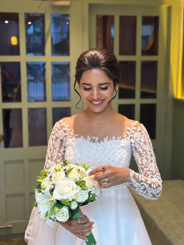 Christian bride in a white lace gown looking down at a white rose bouquet