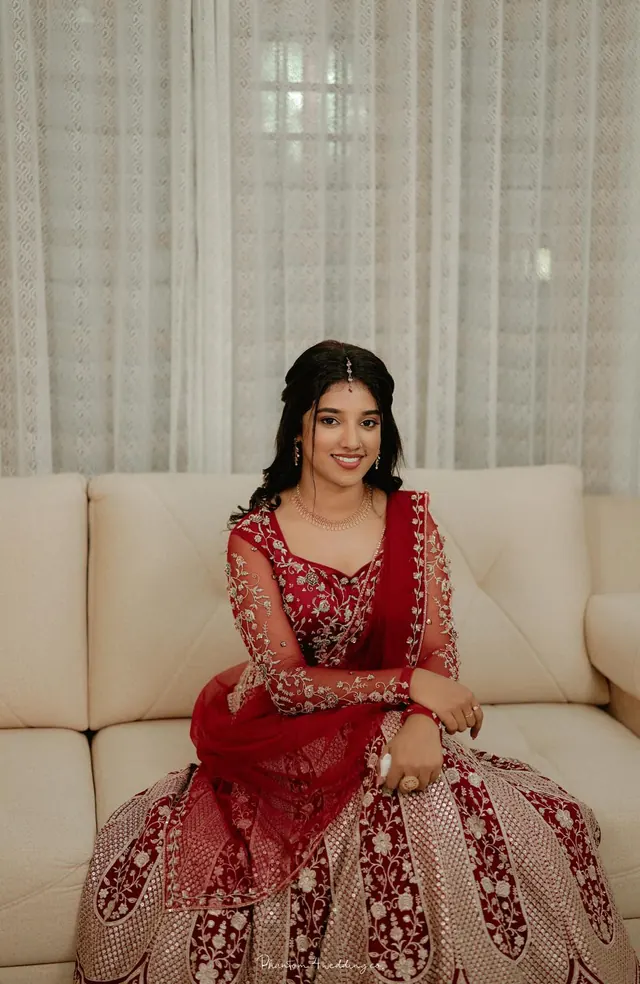 Smiling bride in a red embroidered lehenga seated on a cream sofa